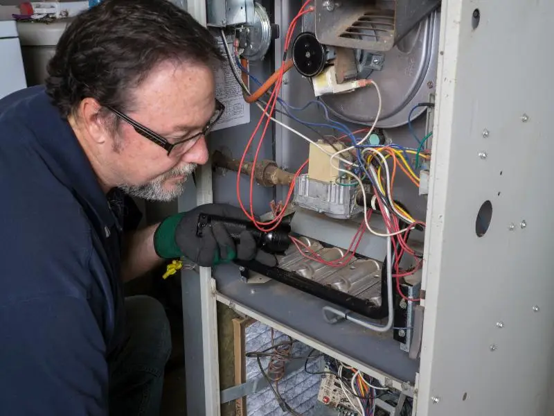Technician inspecting burners and heat exchanger during a furnace replacement diagnostic by Don's in Oakland County